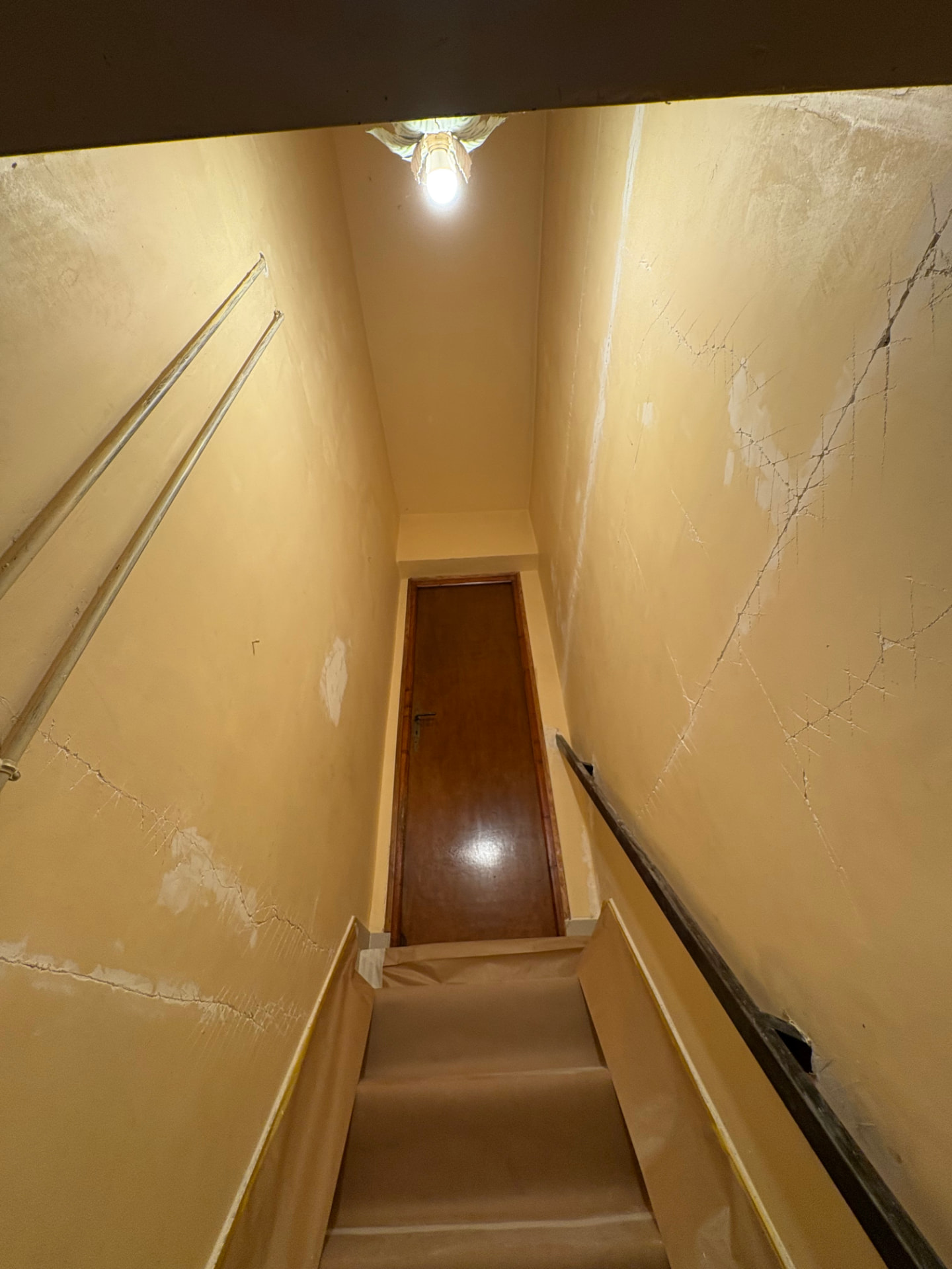 Cage d'escalier aux murs jaunis parcourus de fissures avant travaux