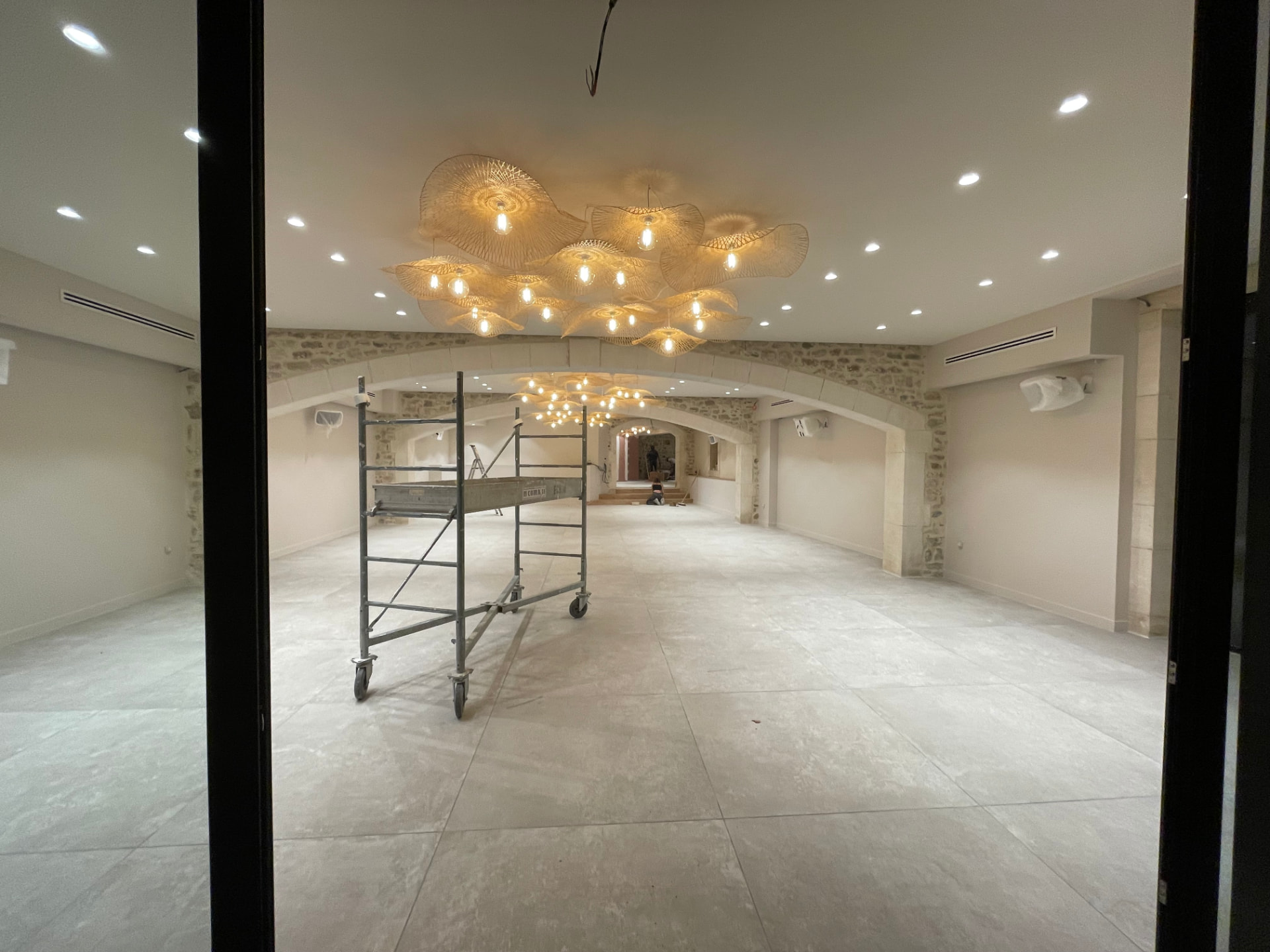 Grande salle voûtée en pierre rénovée avec murs peints en blanc cassé et luminaires en fibre